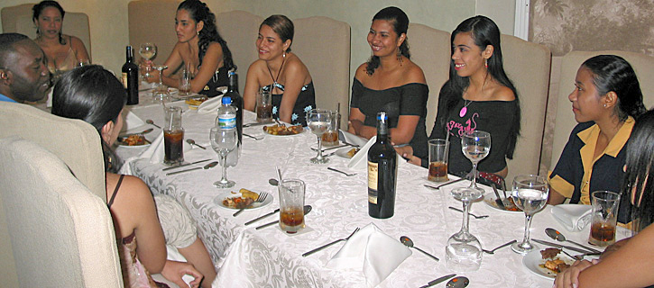 Lunch with Colombian Women A Black man enjoys lunch with Colombian women around a large wooden table with wine and pastries during a formal matchmaking introduction
