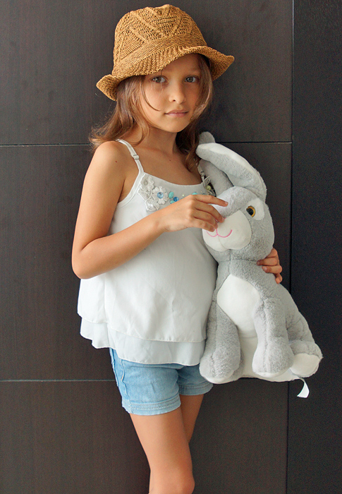 Beautiful young girl in summer clothes and a hat hold a stuff bunny rabit