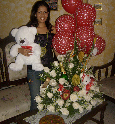 A Colombian woman receiving beautiful flowers, fruits, chocolate, cake, ballons, teddy bear and wine as a gift