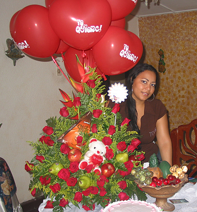 A Colombian woman receiving beautiful flowers, fruits, chocolate, cake, ballons, teddy bear and wine as a gift