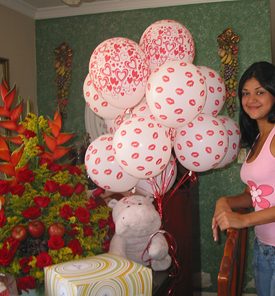 A Colombian woman receiving beautiful flowers, fruits, chocolate, cake, ballons, teddy bear and wine as a gift