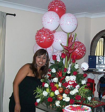 A Colombian woman receiving beautiful flowers, fruits, chocolate, cake, ballons, teddy bear and wine as a gift