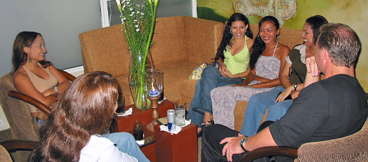 Colombian Women Meet American Man in Lounge Setting An American man meets five smiling Colombian women sitting together on sofas in a casual lounge during an introductory matchmaking event