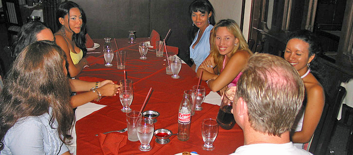 Dinner Conversation with Colombian Women A man speaks with Colombian women around a table covered in a red tablecloth and glasses during a relaxed matchmaking dinner gathering