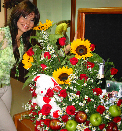 A Colombian woman receiving beautiful flowers, fruits, chocolate, teddy bear and wine as a gift