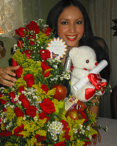 A Colombian woman receiving beautiful flowers, fruits, chocolate, teddy bear and wine as a gift