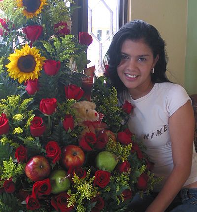 A Colombian woman receiving beautiful flowers, fruits, chocolate, teddy bear and wine as a gift