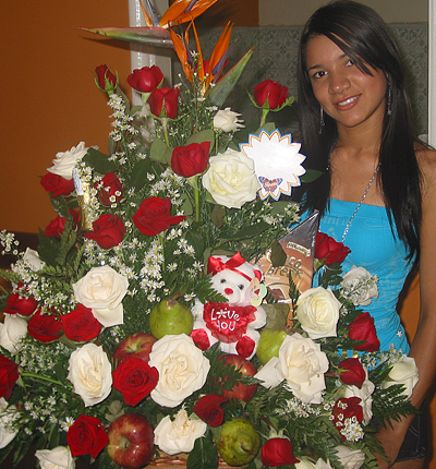 A Colombian woman receiving beautiful flowers, fruits, chocolate, teddy bear and wine as a gift