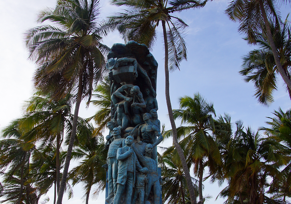 A blue statue representing historical figures of La Guajira with palm trees in the background