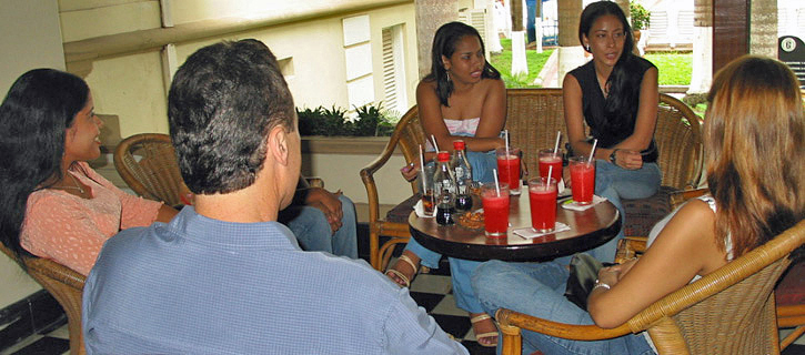 Group Introduction With Latina Women and One Man Group of Latina women and one man sitting together at a table with drinks, talking casually in a relaxed social setting