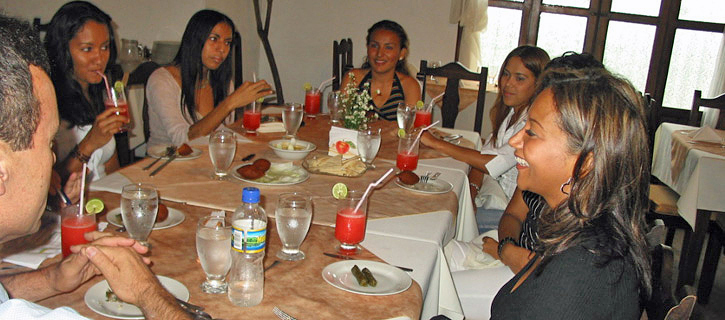 Social Meetup With Latina Women at Restaurant Table Several Latina women seated at a restaurant table with drinks and food, engaged in friendly conversation with a man during a group introduction