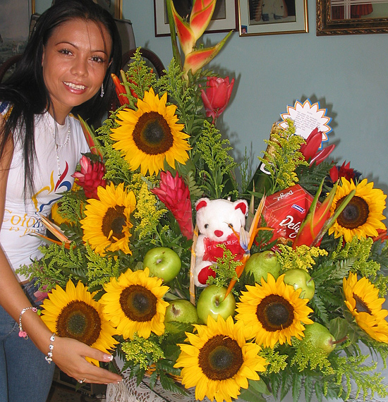 A Colombian woman receiving beautiful flowers, fruits, chocolate, teddy bear and wine as a gift