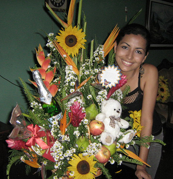 A Colombian woman receiving beautiful flowers, fruits, chocolate, teddy bear and wine as a gift