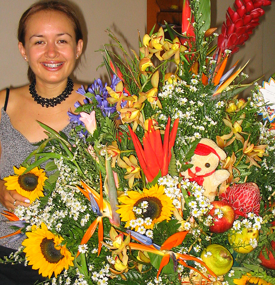 A Colombian woman receiving beautiful flowers, fruits, chocolate, teddy bear and wine as a gift