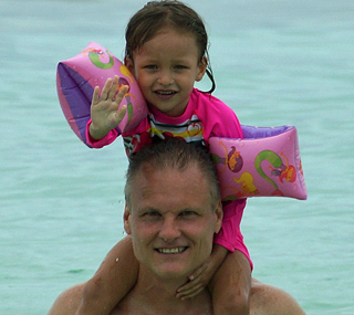 Jamie, the owner of International Introductions a renown marriage agency in South America with his young daughter on his shoulders in the ocean