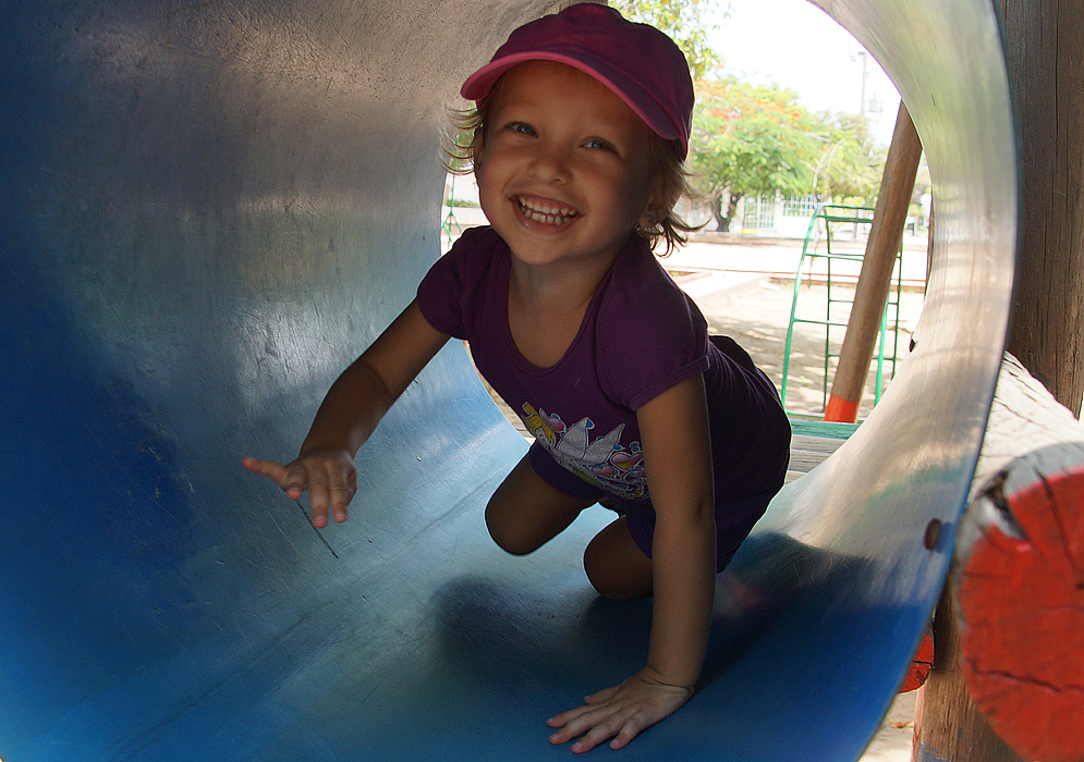 An exuberant toddler crawling inside a playground tunnel