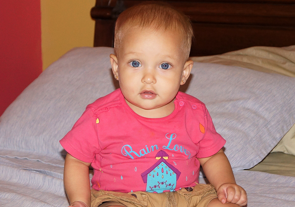 Beautiful baby sitting on bed staring with her brilliant blue eyes