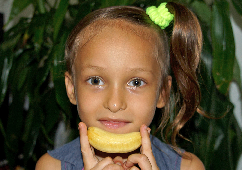 Child Holding a Baby Banana An attractive five-year old girl hold a baby banana horizontally below her mouth