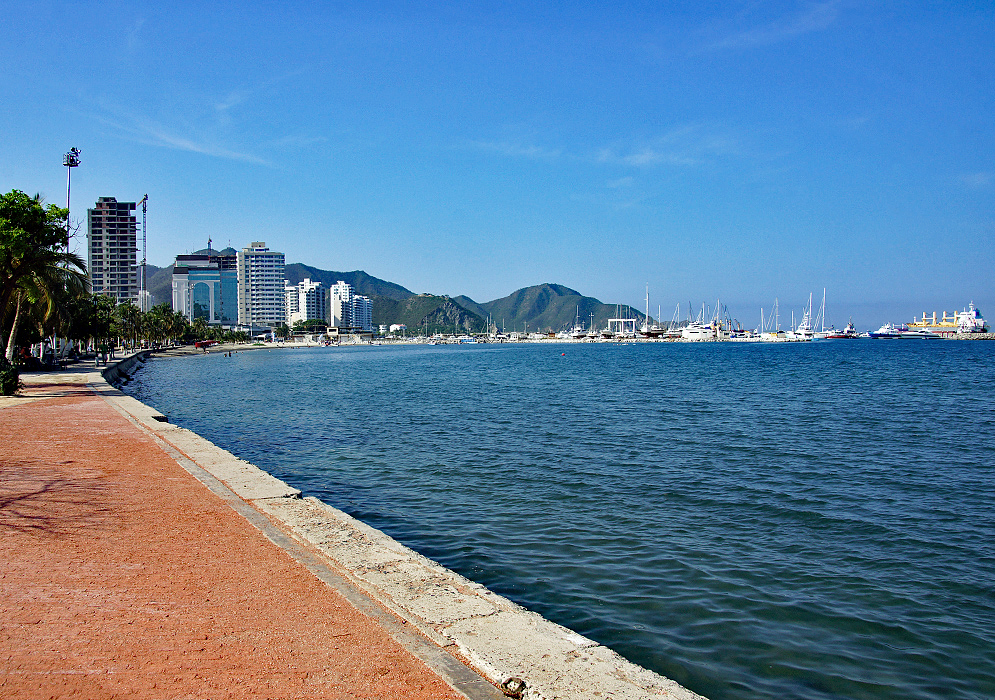 Beach walkway leading to the boat harbor with green mountains in the background and blue skies