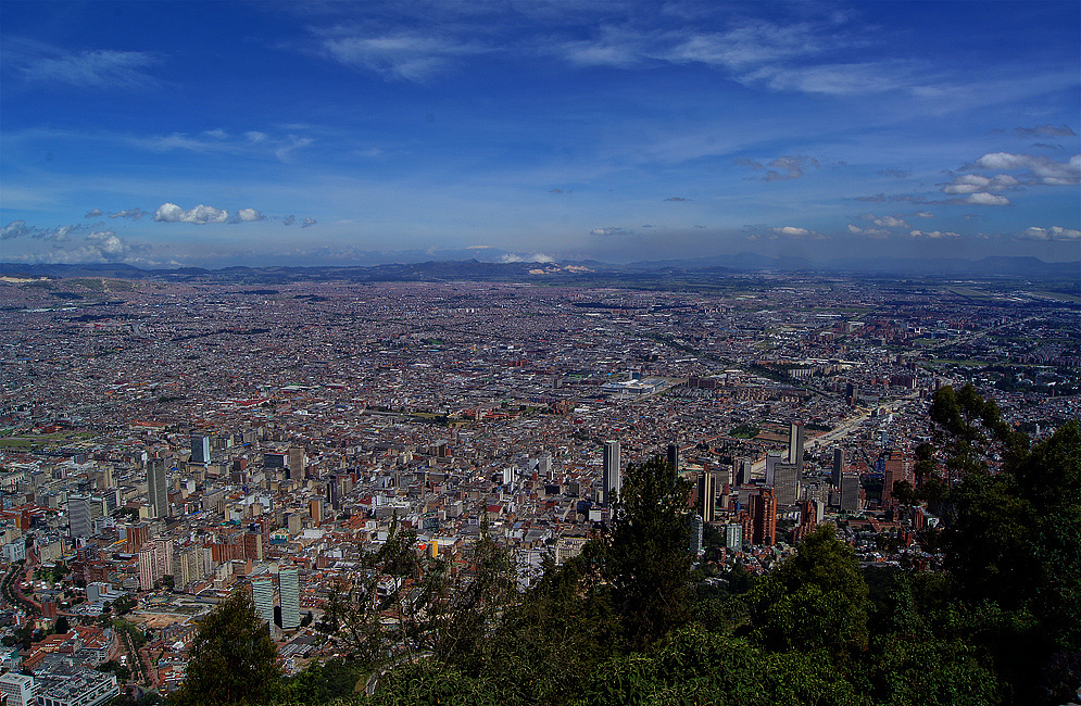 A vista of Bogotá under dark blue skies with a snow-cap mountain in the central Andes in the background
