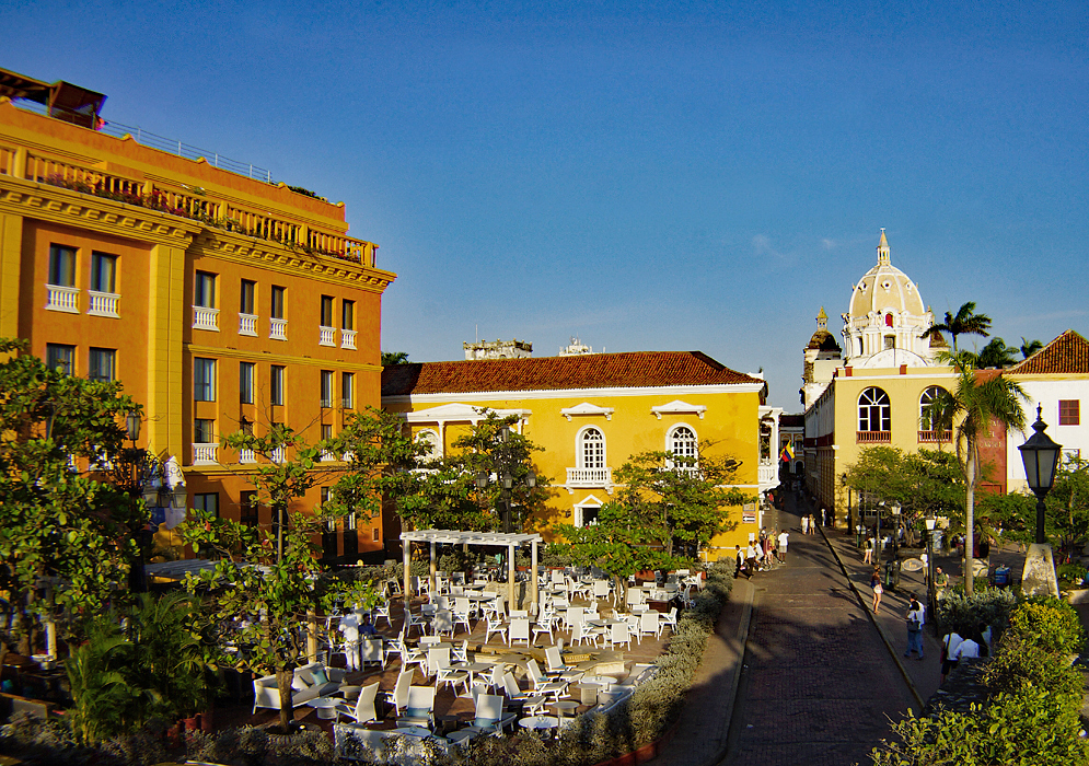 A large dining plaza surrounded by orange and yellow buildings during the late afternon
