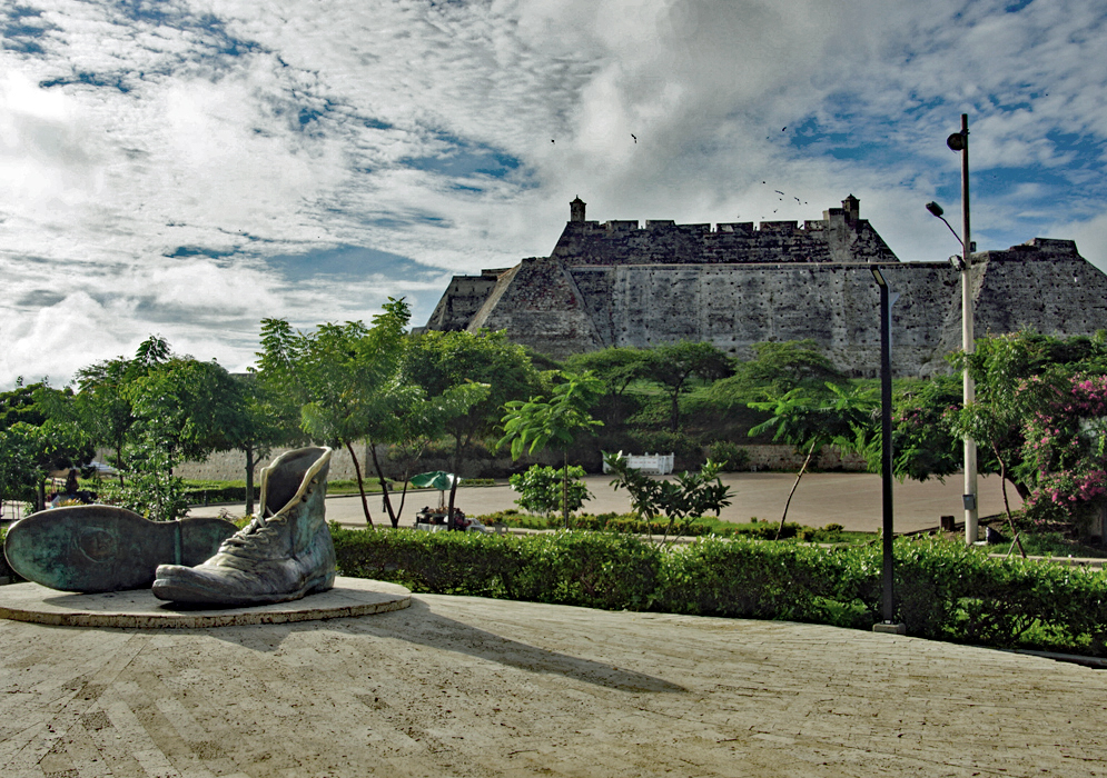 A statue of two large shoes in front of an historical fort