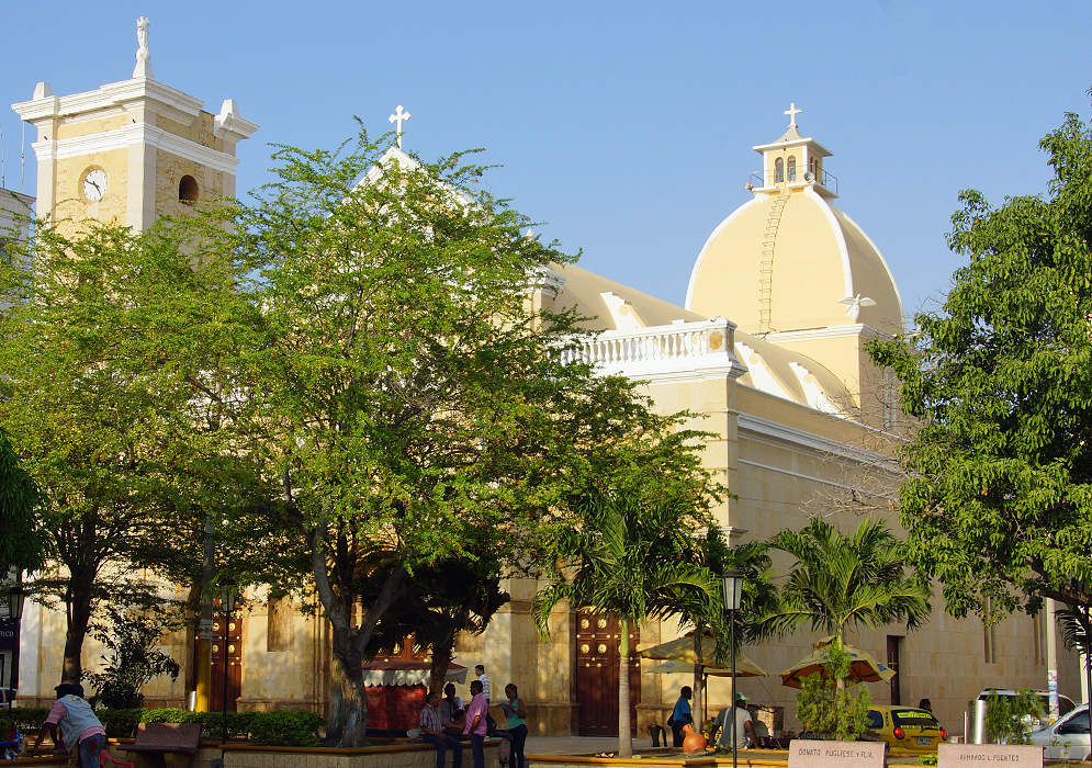 A cathedral behind green trees under blue skies 