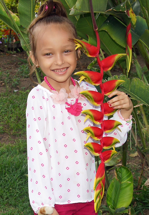 Happy little girl holding on to a long red and yellow Heliconia inflorescence