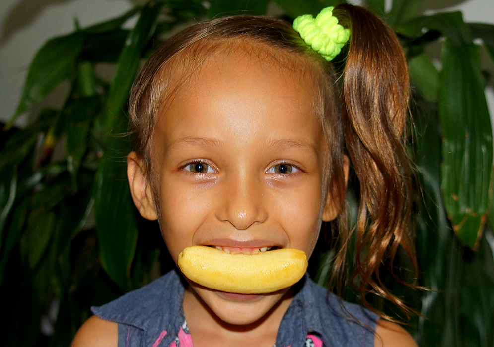 A five-year old girl with a horizontal baby banana in her mouth