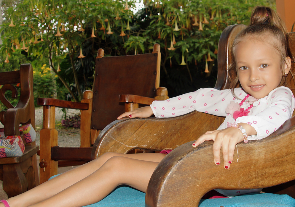 Five year old girl sitting in a wooden chair with a Brugmansia insignis tree in the background