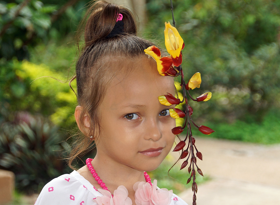 A little girls face behind yellow and red hanging flowers