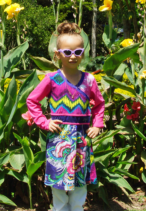 Wearing purple sunglasses and a long colorful shirt the flowers behind her pale in comparison the pretty girls outfit