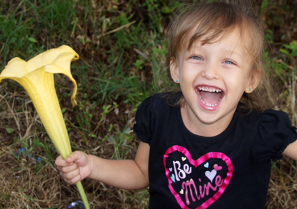 Little girls with mouth wide open hold a large flower and looking up