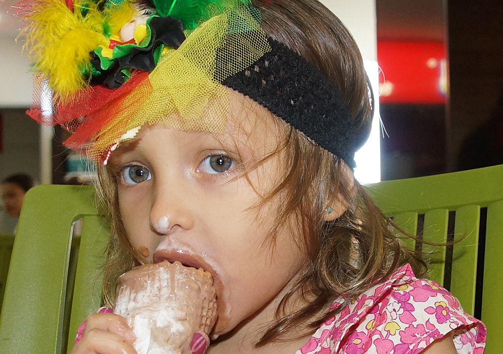 Beautiful three old with an ice cream cone in her mouth and ice cream on her face