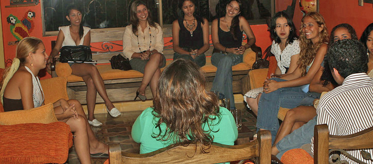 Group of attractive Colombian women sitting together and conversing with a man during an organized introduction event in a Colombian-style lounge