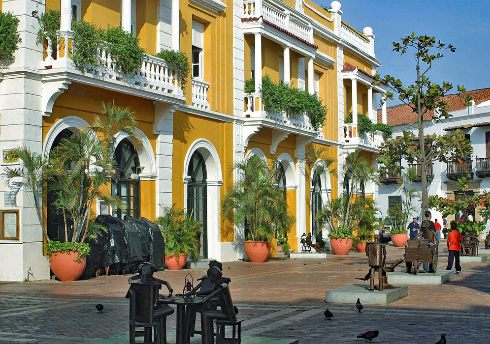 A yellow and white building inside the old city with metal statues are on display in front