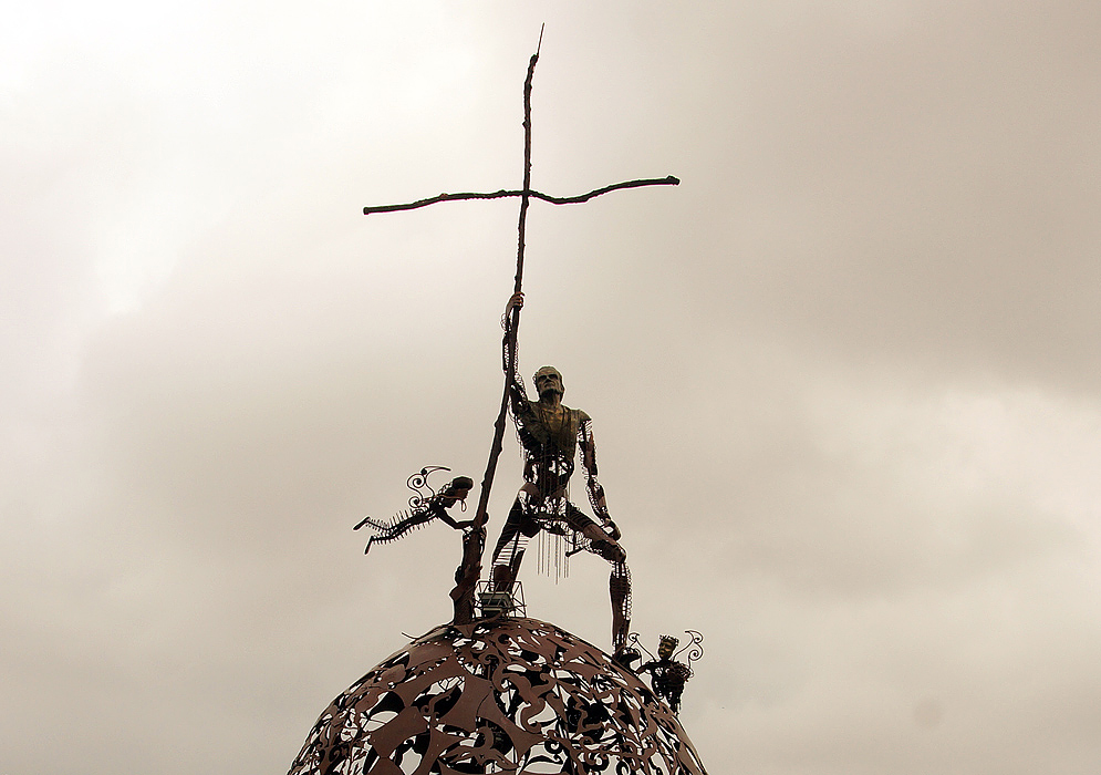 A man made of metal holding a cross