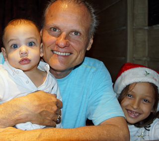 Jamie, dad and owner of International Introductions hugs his baby son Derick Quinn and daughter Danica Alejandra in a Santa hat; all smiles
