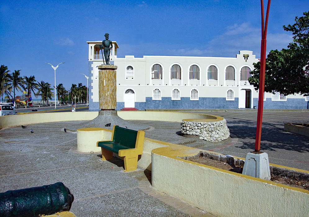 A church near a beach with a small plaza and a statue under blue skies