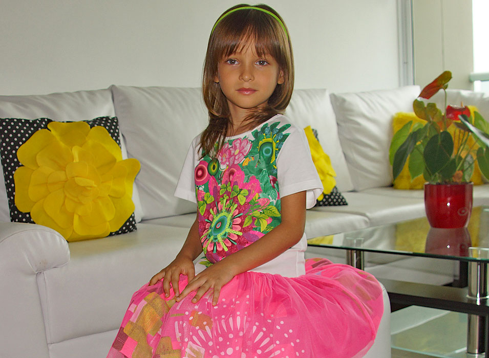 Eloquent five year old sitting-up straight on a white sofa stool with her pink skirt spread-out on display