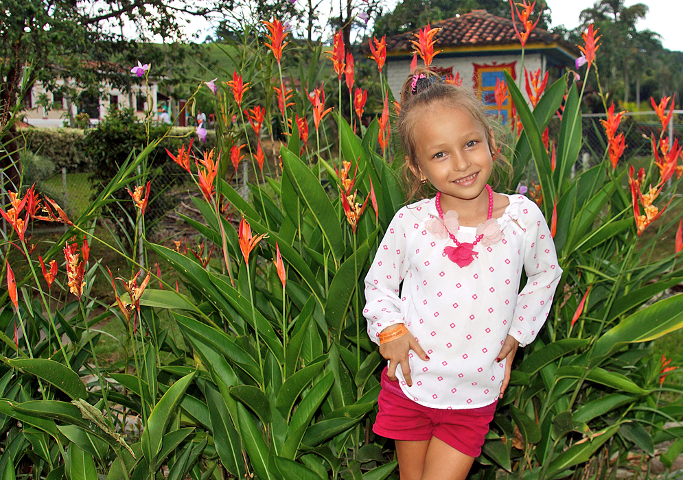 Pretty smiling blond five-year old wearing pink and white clothes in front of Heliconia psittacorum plants