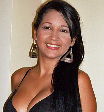 Smiling Latina Woman with Long Black Hair Beautiful Latina woman with long straight black hair wearing large triangular earrings and a black dress, smiling confidently while posing indoors against a beige wall