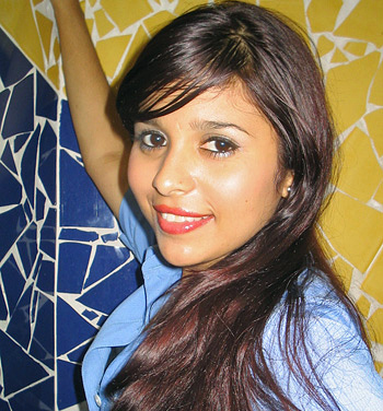 Smiling Latina Woman in Blue Shirt Young Latina woman with long reddish-brown hair wearing a light blue blouse, smiling brightly while standing against a colorful tiled wall