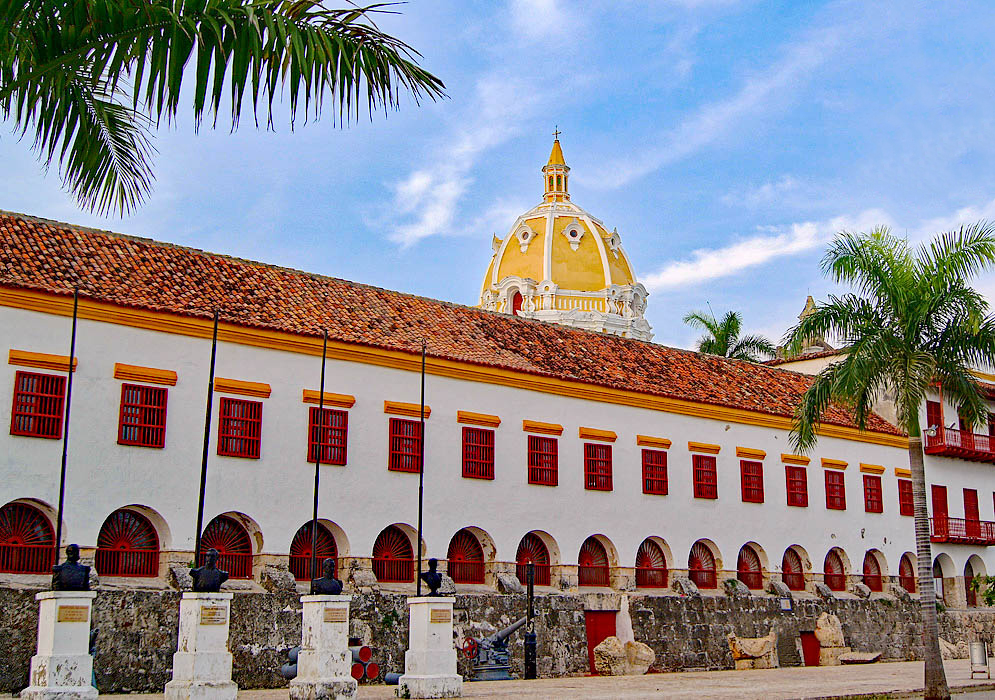 A long white building with arches facing outside of Old Town with statures in front of the building