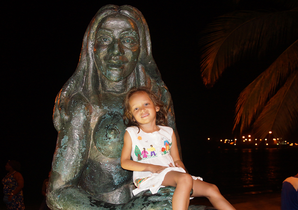 Four year old girl sitting next to an Indian statue at night in Santa Marta