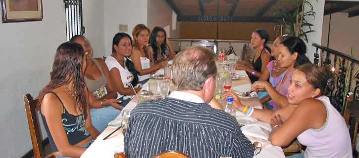 Restaurant Introduction Meeting A man sits across from several Colombian women during a group introduction dinner in a bright restaurant with white walls and casual conversation