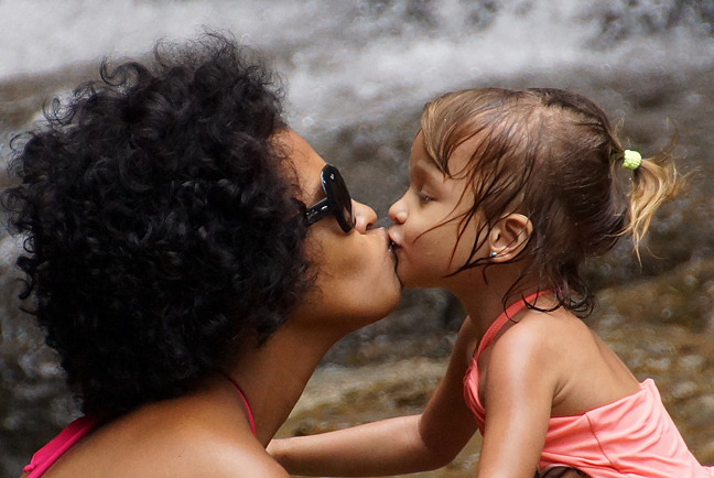 Mom and her two year old daughter kissing in front of a waterfall