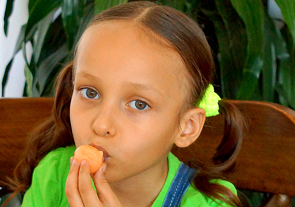 An attractive five-year old girl with an orange mamón near her mouth