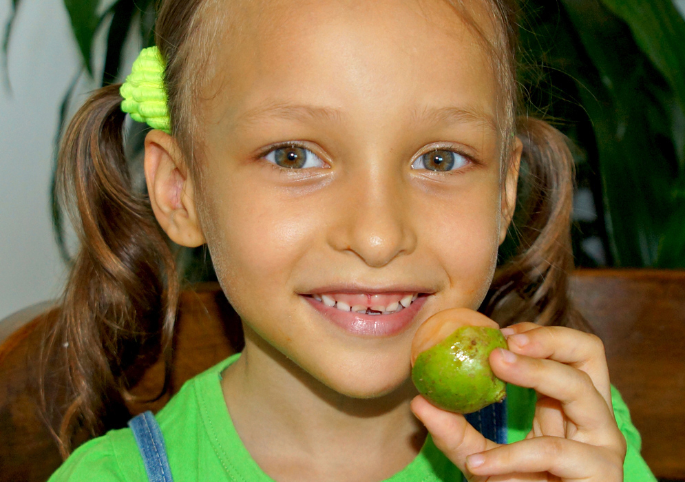 A beautiful five-year old girl with a half open green and orange mamón in her hand