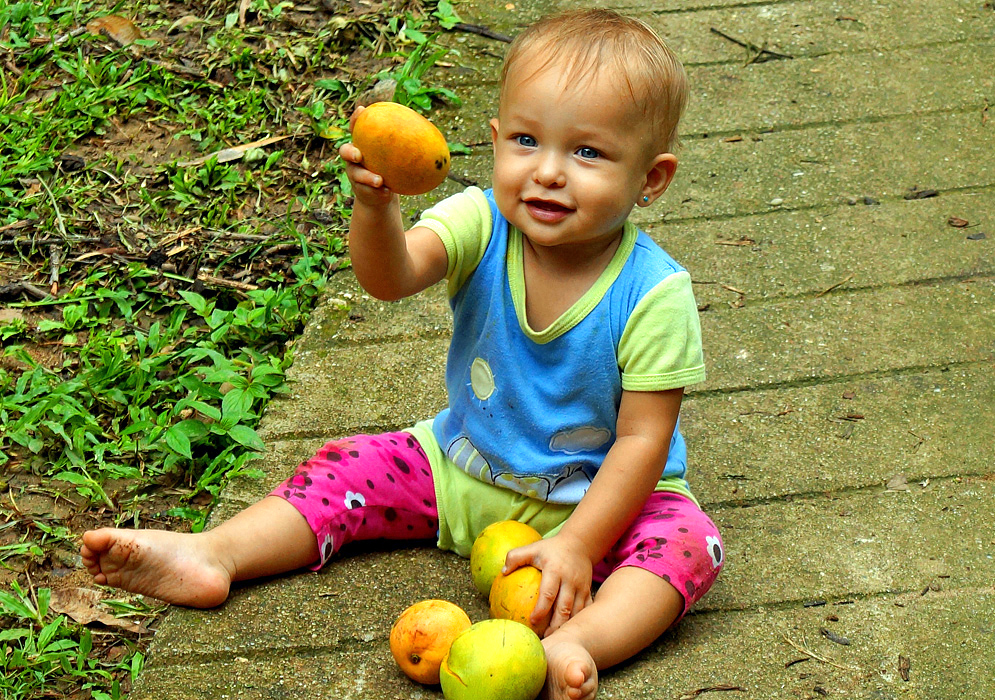 Beautiful smiling one year old girl holding up a mango